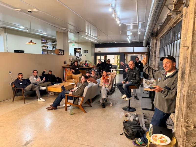 Group of about 15 people gathered in a loft-style space for a Claude Code Show and Tell meetup, with one person standing at the right hosting the session